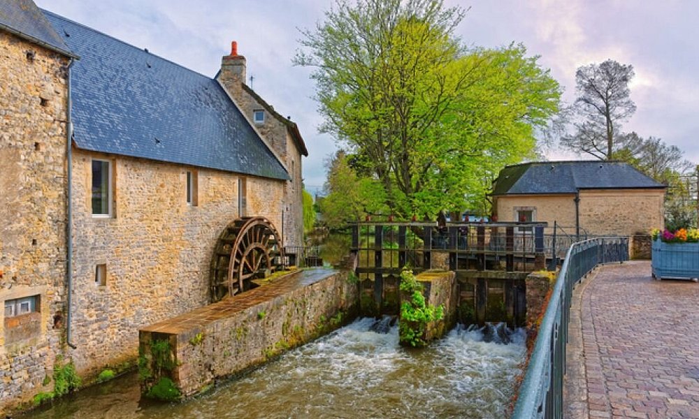 A historic stone watermill and waterwheel beside the River Aure in Bayeux